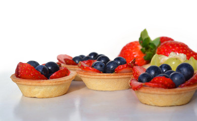 Mini fruit tarts with grape and strawberry slices on gray kitchen counter.