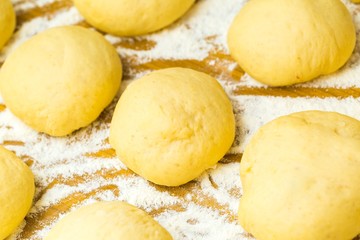 Raw donuts lying in flour on wooden table