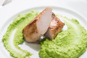 Detail of grilled chicken steak with mashed green peas up on a plate