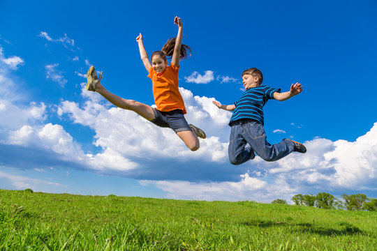 Two kids jumping on green hills