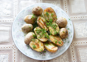 Russian Traditional baked potatoes with the peel and fennel, drizzled with oil on a plate with a gray ornament