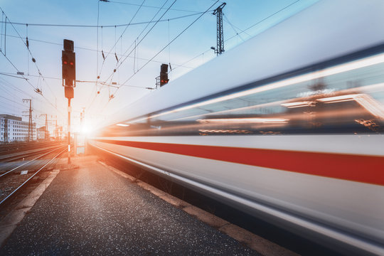 Fototapeta Modern high speed passenger train on railroad in motion at sunset. Blurred commuter train. Railway station at dusk with vintage toning. Travel background, railway tourism. Industrial landscape. Train