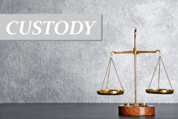 Scales of justice on table. Word CUSTODY on background