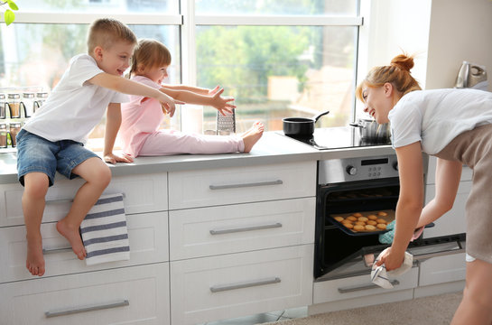 Young mother and kids tasting biscuits in kitchen