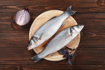 Raw fish with onion and basil on wooden background