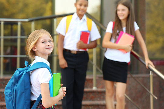Cheerful teenagers with backpacks and notebooks standing on school stairs