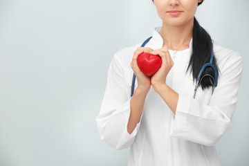 Female doctor with stethoscope holding heart, on light background