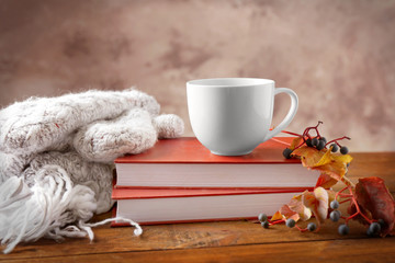 Books with cup of tea, scarf and autumn leaves on wooden table