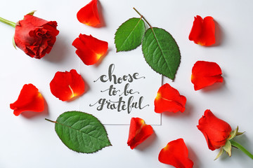 Quote "Choose to be grateful" written on paper with petals and leaves on white background. Top view
