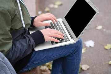 Fototapeta premium Teenager sitting on parapet with laptop in autumn day, close up