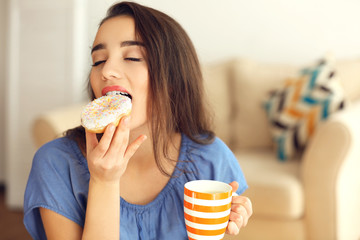 Beautiful young woman with tasty donut and cup of coffee on blurred background