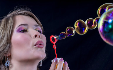 Fototapeta premium a girl with bright makeup blows soap bubbles. on a black background.
