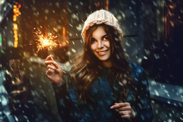 Outdoor photo of young happy smiling girl holding sparkler, walking on street. Model looking at...
