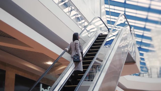 Full length of confident businesswoman standing on escalator with laggage in airport. Business woman with suitcase in mall.