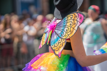 Young woman in a crowd celebrating Pride Parade. Wearing colorful rainbow butterfly wings and a...