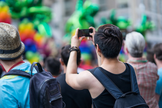 Man in the crowd celebrating Pride Parade. Taking a picture of the festivities with his mobile phone. During a march supporting marriage equality and LGBT rights.