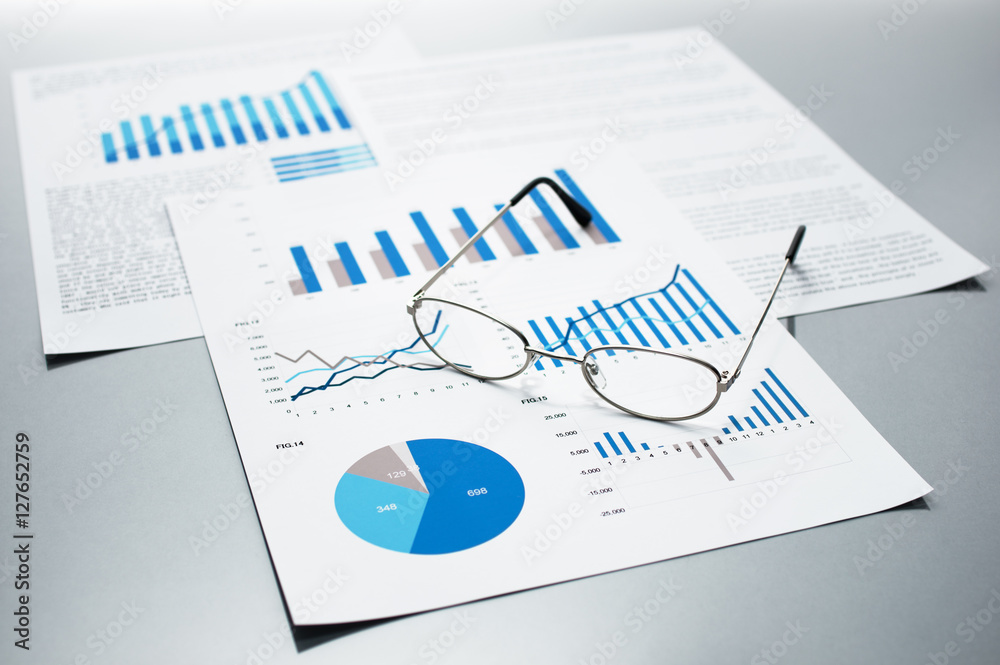 Poster Checking business reports. Graphs and charts. Documents and glasses on gray reflection background.
