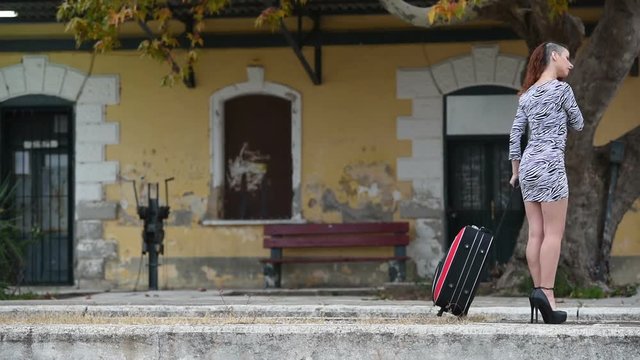 Slim woman walking front of a traditional train station pull a huge bag on wheels