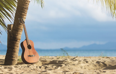 Fototapeta premium An acoustic guitar standing in the sandy beach under palm tree