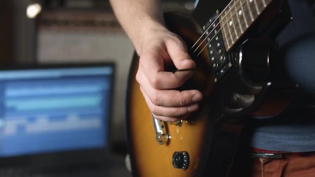 Session musician play lead guitar solo with plectrum and record result with laptop