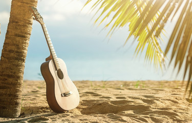 An acoustic guitar standing in the sandy beach under palm tree