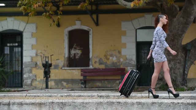Slim woman pull huge bag on wheels front of a traditional train station