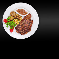 Grilled steak, baked potatoes and vegetables on white plate on black background.