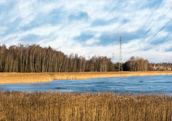 Power line over icy water on a sunny winter day with dry reeds in the foreground