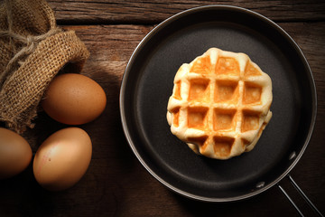 Baked waffles inside the teflon pan and eggs on wood background