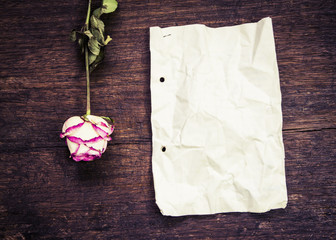 old paper with dry rose on wooden background, copy space