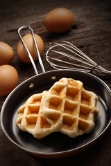 Close up baked waffles inside the teflon pan with hand mixer kitchen and eggs on wood background