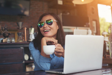 Pretty young hipster woman sitting in a cafe with her laptop, lo