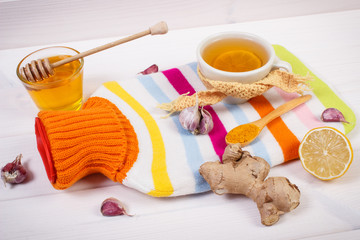 Hot water bottle, cup of tea and ingredients for preparation warming beverage