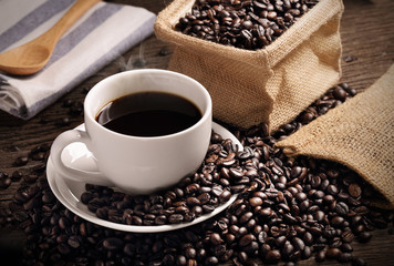 warm cup of coffee with sack inside by coffee bean on wood background