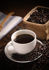 warm cup of coffee with sack inside by coffee bean on wood background