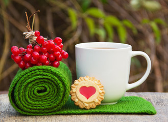 A cup of hot tea, warm knitted scarf, and a bunch of red viburnum. Home comfort. Autumn concept, romantic concept. Homemade cookies in the shape of a heart.