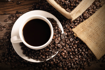 warm cup of coffee with sack inside by coffee bean on wood background