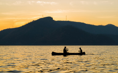 silhouette of two men are boating in the dam on the morning.