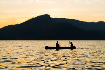 silhouette of two men are boating in the dam on the morning.