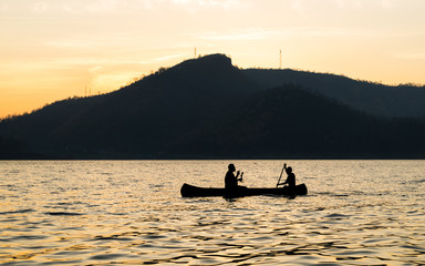 silhouette of two men are boating in the dam on the morning.