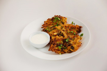Fried brown potato pancakes with cup of cream on plate isolated