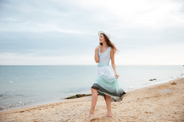 Fototapeta na wymiar Woman in white hat and dress walking on the beach