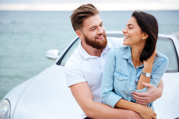 Obraz premium Young couple embracing while standing near car at the seaside
