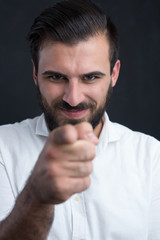 Portrait of a  young bearded man pointing to camera against blac