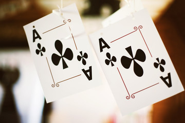 Two clubs aces playing cards are hanging at blurred background.