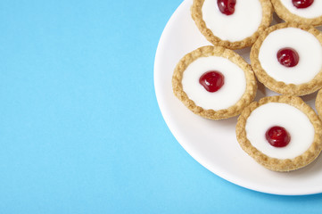 A plate full of freshly baked Bakewell tarts on a bright blue background with empty space at side