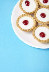A plate full of freshly baked Bakewell tarts on a bright blue background with blank space below
