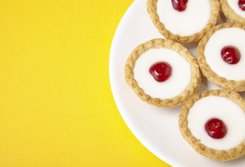 A plate full of freshly baked Bakewell tarts on a bright yellow background with blank space at side