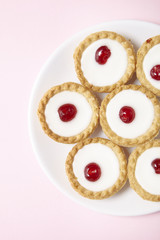 Overhead view of a plate full of freshly baked Bakewell tarts on a pastel pink background