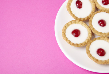 A plate full of freshly baked Bakewell tarts on a hot pink background with empty space at side